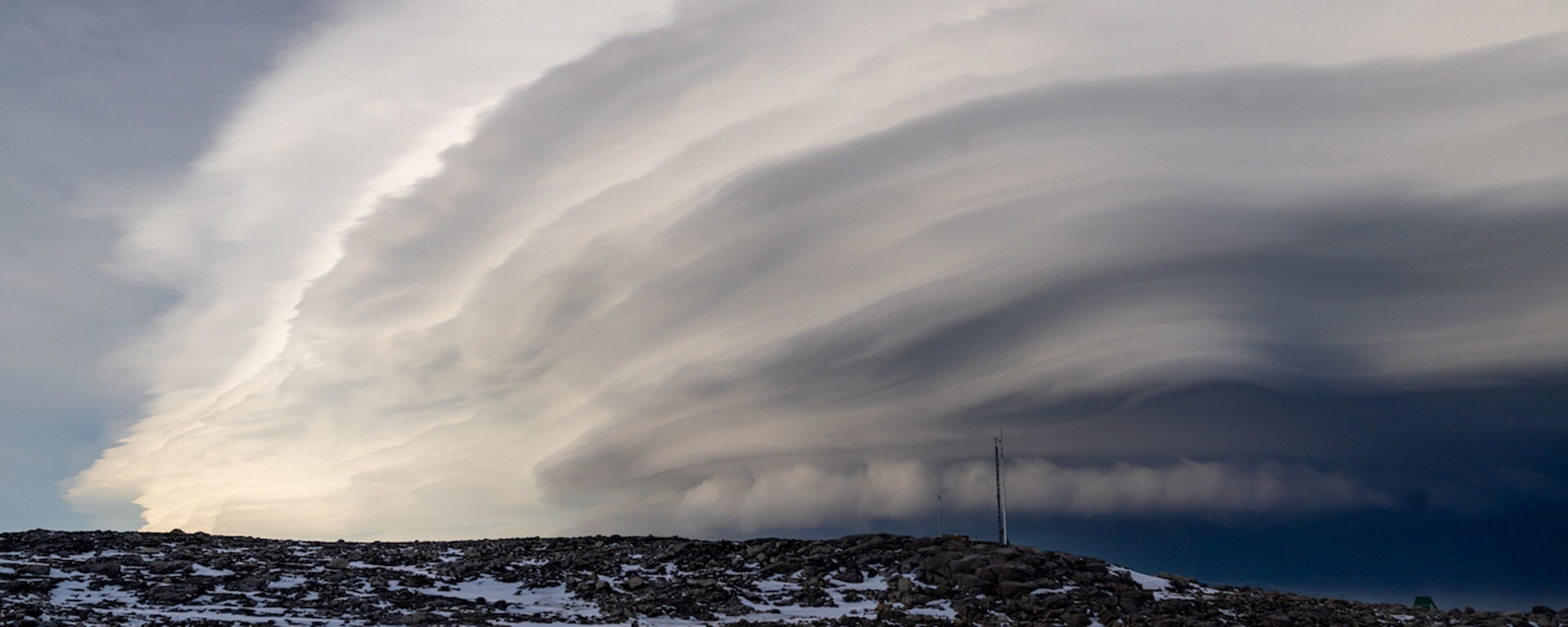 A cloud formation reaching a very great height in the sky. It has many wavelike layers, all seeming to converge downward to a point on the horizon.