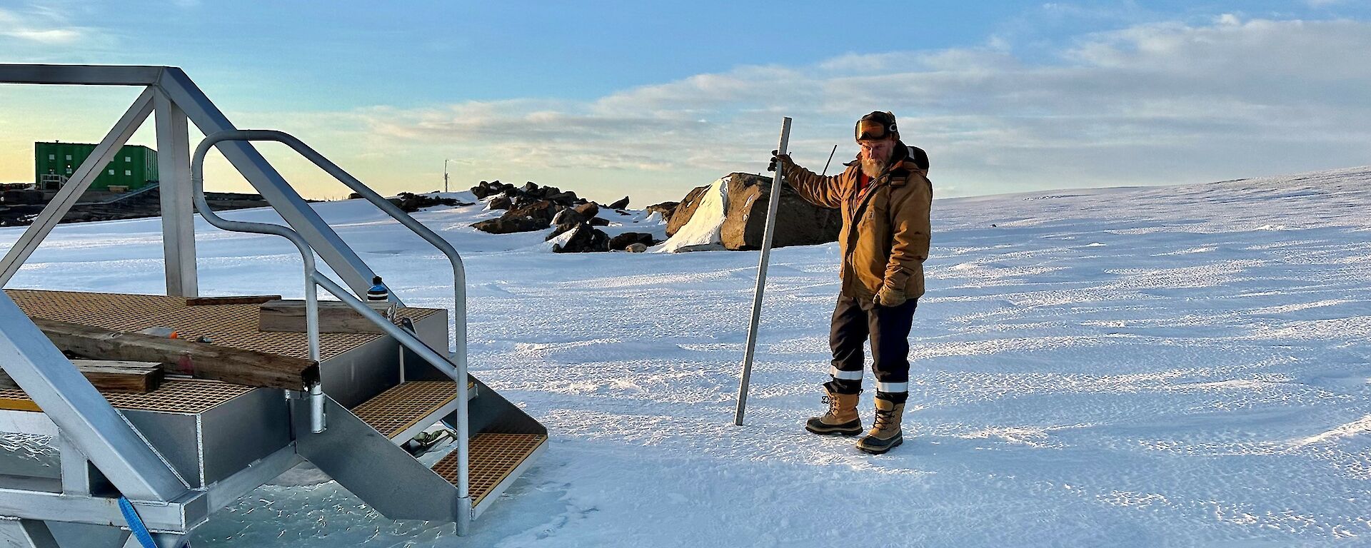 A man stands on a snowy slope with stairs to the left