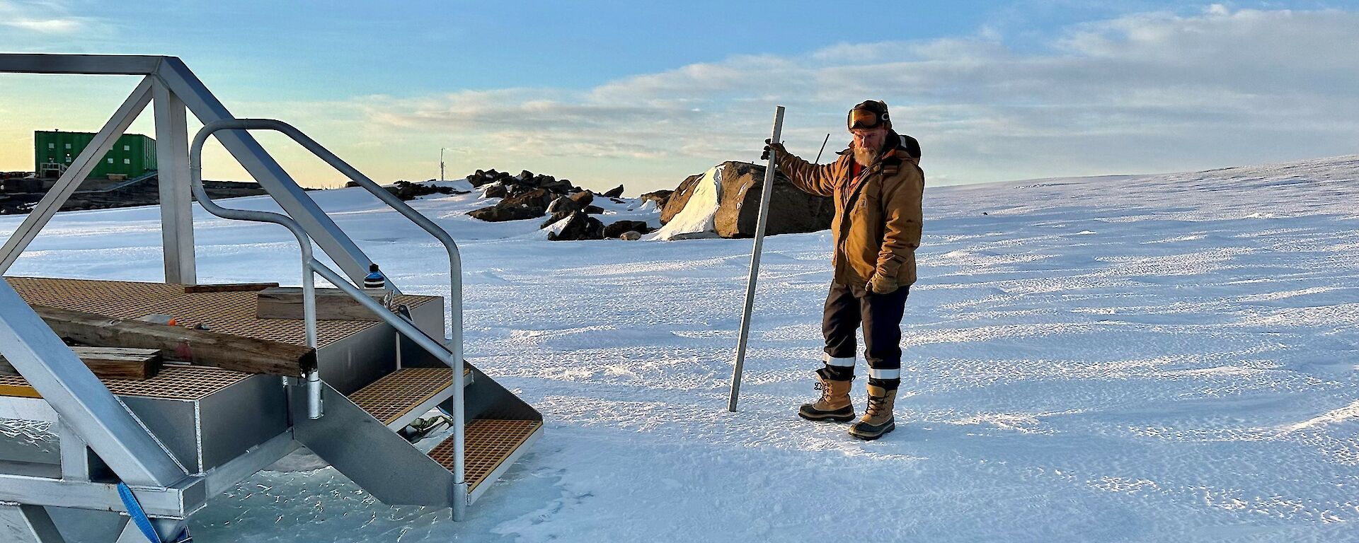 A man stands on a snowy slope with stairs to the left