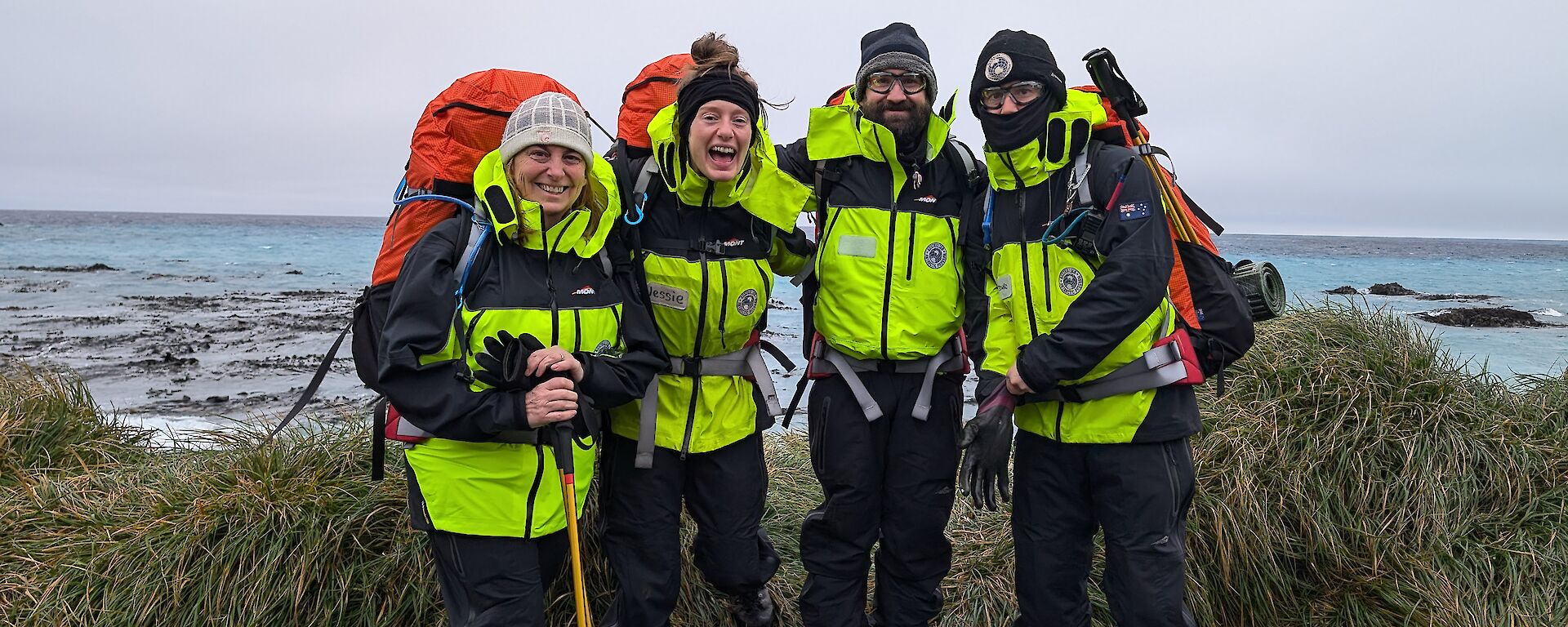 Four people in outdoor gear stand on a gravel road with the sea behind them