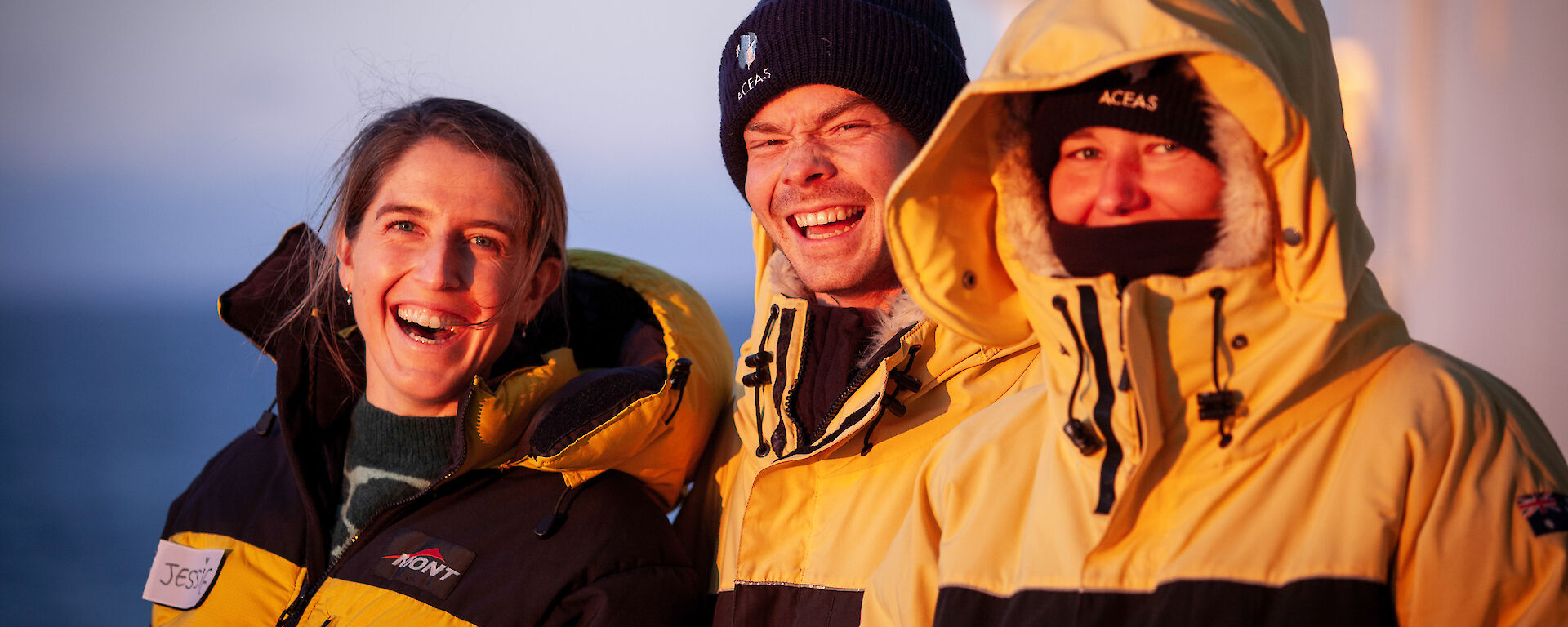 3 expeditioners dressed in their Antarctic clothing smile at the camera