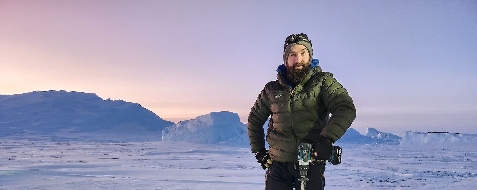 An expeditioner on the sea ice with a drill and attachment, checking the depth of the ice