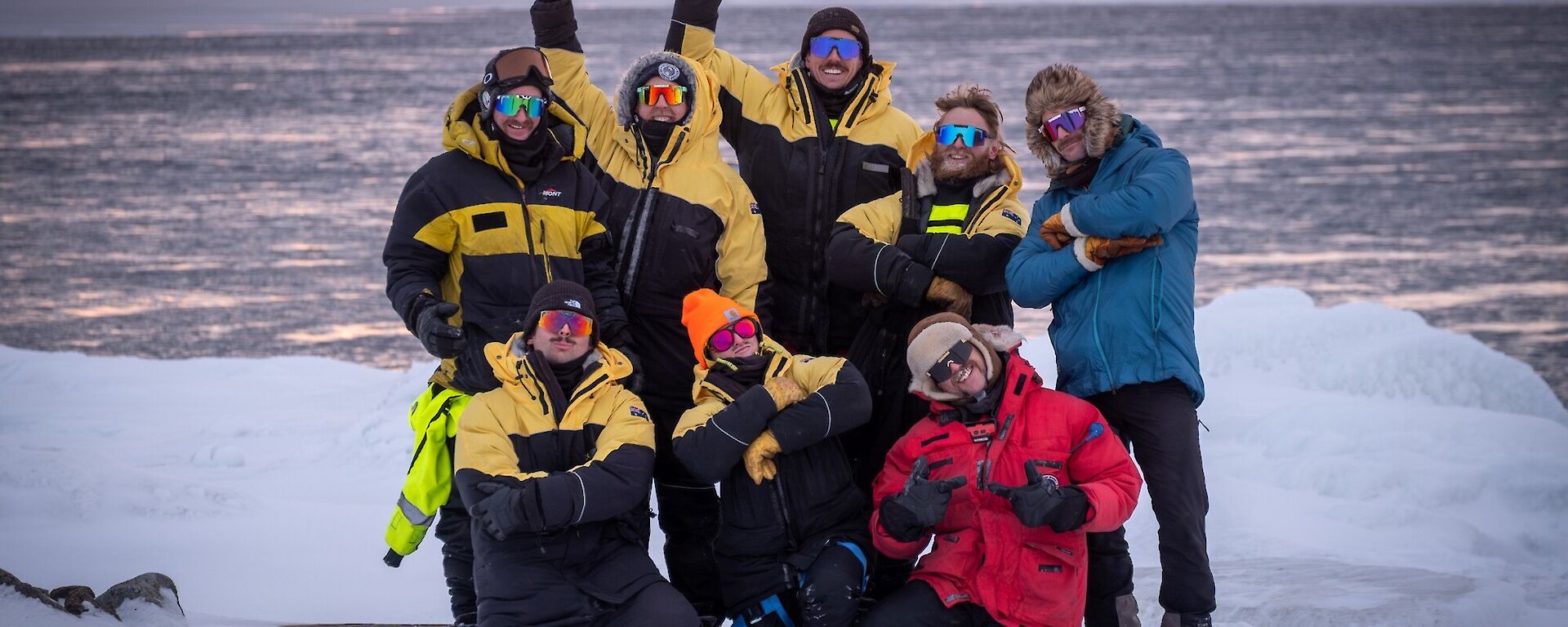 A group of people posing for the camera standing on ice with water behind