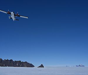A twin otter aircraft flying over the ice, with jagged mountain peaks in the distance.