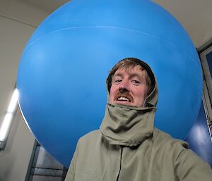 A man wearing a khaki brown protective jacket is standing in front of a large blue balloon