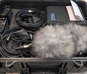 A black hard case contains a number of cables and a fluffy grey microphone