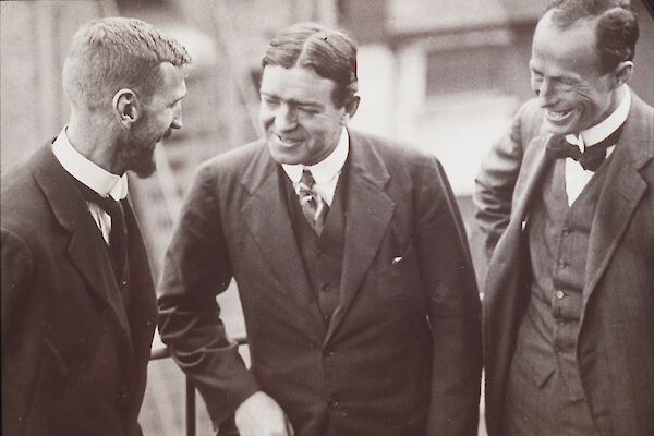 Black and white photo of three men in three-piece suits, talking and smiling