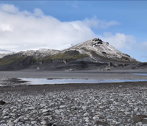 A rocky peak rises into a blue sky with som elow cloud behind.