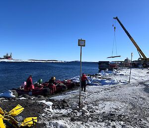 Small boats in the water with a crane on snowy land to the right