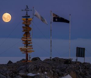 Full moon shining over the signage and Australian flag at Casey Station