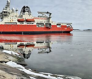 Nuyina positioned just off Mawson's West Arm during refuelling operations, with fuel hose and small boat in the water