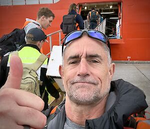 A selfie of an expeditioner giving the 'thumbs up' as others board the RSV Nuyina at Hobart's Macquarie Wharf