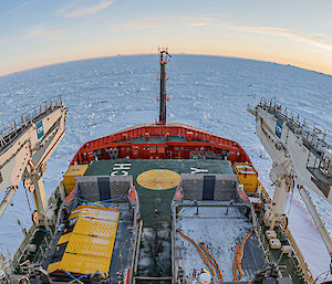 A fish-eye lens view of the front of the Nuyina, pushing through pack ice with sun in the background
