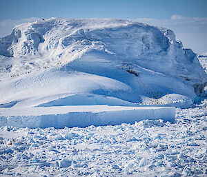 A large iceberg surrounded by sea ice, with lines of Adelie penguins walking on it