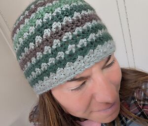 A woman tries on a stripey grey, bottle green and brown beanie