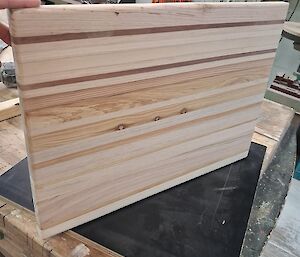 A multi layered wooden chopping board made of scrap timber with alternating layers of dark and light wood.