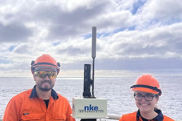 Two Bureau of Meteorology expeditioners standing next to a CSIRO ARGO float on the helo deck of Nuyina.