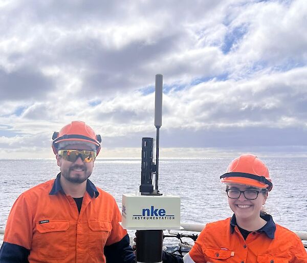 Two Bureau of Meteorology expeditioners standing next to a CSIRO ARGO float on the helo deck of Nuyina.