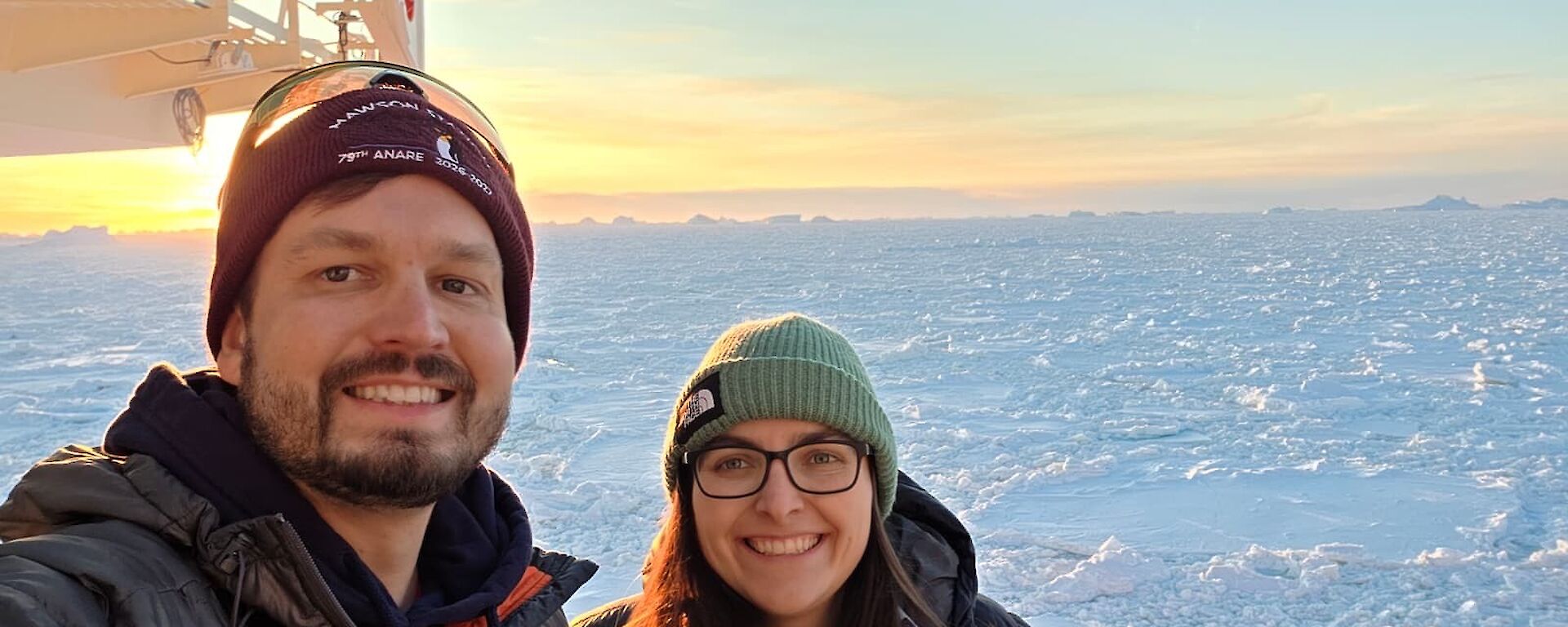 Two expeditioners taking a selfie on outer deck of Nuyina, with sea ice in the background.