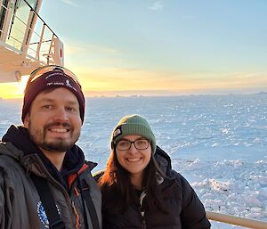 Two expeditioners taking a selfie on outer deck of Nuyina, with sea ice in the background.