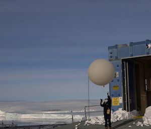 An expeditioner releasing a weather balloon into the sky, in front of Mawson station's balloon building.