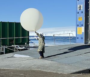 An expeditioner releasing a weather balloon into the sky, in front of Mawson station's balloon building.
