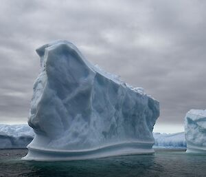 A large iceberg, shaped something like an anvil rises out of the water, with other icebergs in the background.