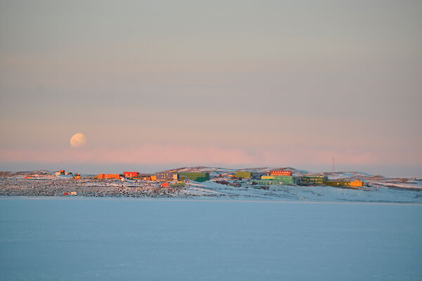 Green, red and yellow station buildings on the snow under a dusky sky with moon