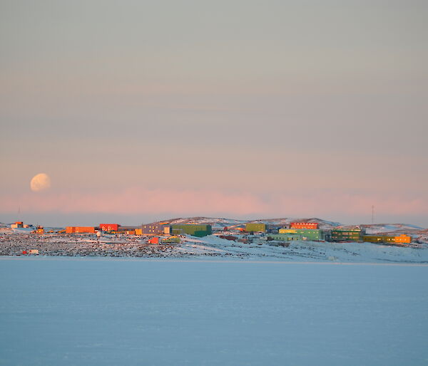 Green, red and yellow station buildings on the snow under a dusky sky with moon