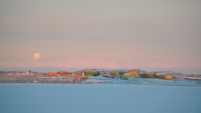 Green, red and yellow station buildings on the snow under a dusky sky with moon