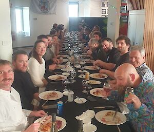 Smiling people sitting down at a long dining table with food in front of them
