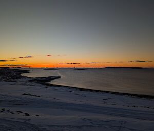 The sun sets over a calm bay with a striking orange stipe of colour just above the horizon