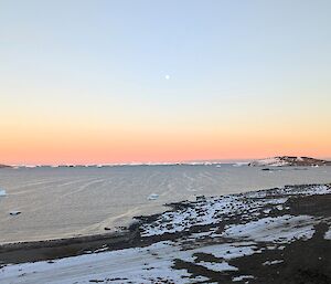 The moon is barely visible in a pale blue sky, with a layer or light orange along the horizon.