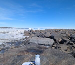 Paint and paper are sitting on a rock in the foreground, with ricks and ice spreading to the horizon, below a very blue sky