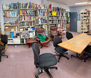 a room with books on shelves, an unfinished jigsaw puzzle on a table and various community amenities like a sewing machine.