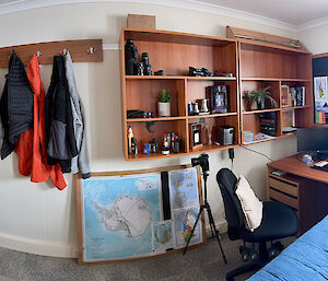 a panoramic view of an expo's room, showing a bed, a window, personal items on shelves and clothes hanging off hooks on walls