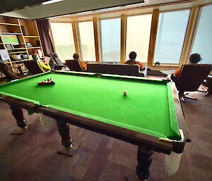 expeditioners sitting on chairs looking out the windows, with a pool table in the foreground