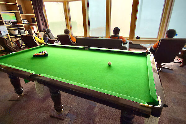 expeditioners sitting on chairs looking out the windows, with a pool table in the foreground