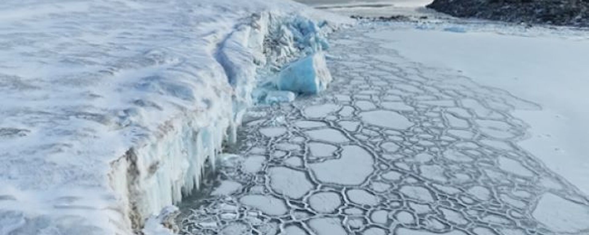 An icy white cliff to the left, above pancake ice on the sea below