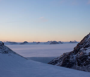 A picture taken on the plateau behind Mawson, with rocky outcrops, mountains and blowing snow