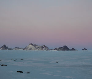A photo of rugged mountain ranges into the distance, taken at sunset where there are purple hues in the sky