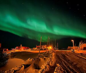 A green aurora stretches above a group of buildings sitting in a snowy landscape