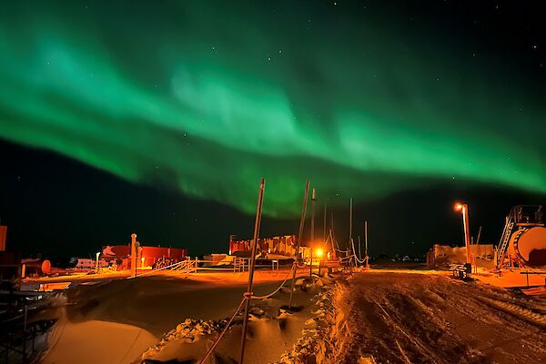A green aurora stretches above a group of buildings sitting in a snowy landscape