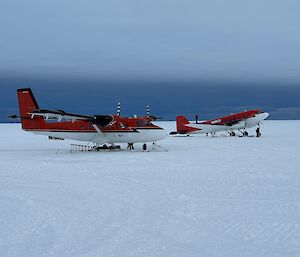 Two red and white planes are parked on an expanse of white ice, under a cloudy grey sky