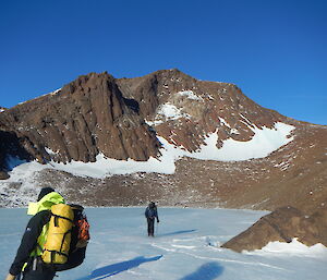 expeditioners on blue sea ice lake, surrounded by rocky mountain features