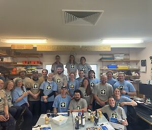 A group of about 20 smiling people wearing blue- or khaki-coloured t-shirts with a penguin image on the front