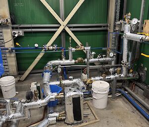 Inside a green building, looking at various site-service water pipes, inlet and outlet lines and valves.
