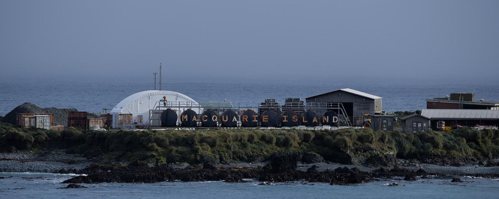 A view of Macquarie Island's sign, written across eight brown fuel drums, from the water.