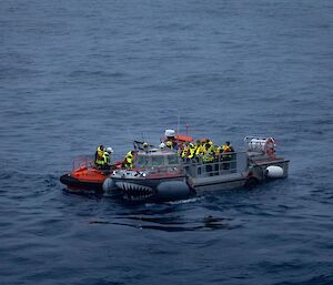 An amphibious vehicle collecting a load of passengers from a small personnel transfer tender.