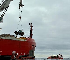 A vehicle being craned off RSV Nuyina on to a barge, while a small boat waits nearby.